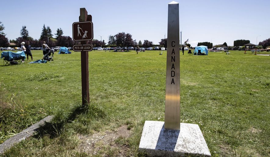 A Canada-U.S. border marker stands in Surrey, British Columbia, as people gather at Peace Arch Historical State Park in Blaine, Wash., Sunday, July 5, 2020. Although the B.C. government closed the Canadian side of the park in June due to concerns about crowding and COVID-19, people are still able to meet in the U.S. park due to a treaty signed in 1814 that allows citizens of Canada and the U.S. to unite in the park without technically crossing any border. (Darryl Dyck/The Canadian Press via AP)