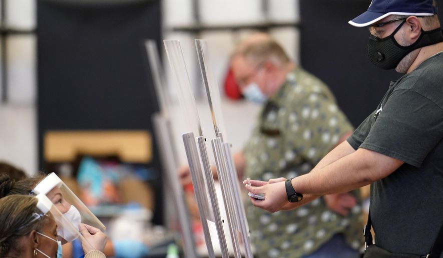 A voter, right, shows his identification to a Harris County election clerk before voting, Tuesday, July 14, 2020, in Houston. (AP Photo/David J. Phillip)