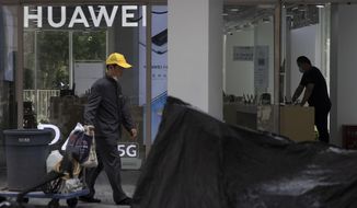 A worker pulls a trolley past a man looking at phones displayed at a Huawei store in Beijing Monday, July 13, 2020. Huawei Technologies reported Tuesday that its revenue grew 13.1% in the first half of the year compared with a year earlier, despite sanctions from the U.S and challenges from the coronavirus pandemic. (AP Photo/Ng Han Guan