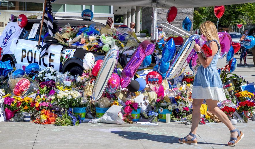A memorial for Bothell Police Officer Jonathan Shoop, killed in the line of duty on Monday evening, grows on top of and around a Bothell Police Car parked at Bothell City Hall on Wednesday, July 15, 2020, in Bothell, Wash. (Mike Siegel/The Seattle Times via AP)