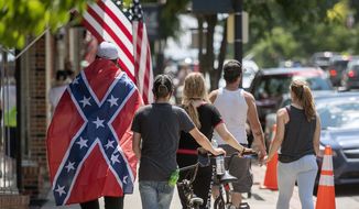 In this July 3, 2020, file photo a man wears a Confederate flag while walking with others in Marion, Va. Defense leaders are weighing a new policy that would bar the display of the Confederate flag at department facilities without actually mentioning its name, several U.S. officials said Thursday, July 16. Officials said the new plan presents a creative way to ban the Confederate flag in a manner that may not raise the ire of President Donald Trump, who has defended people’s rights to display it. (Andre Teague/Bristol Herald Courier via AP, File)