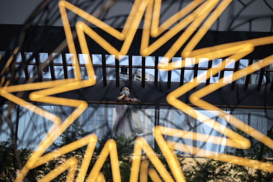 A woman wearing a mask to curb the spread of the coronavirus is framed by lights at a mall in Beijing, China on Tuesday, July 14, 2020. Health experts have warned that outbreaks that had been brought under control with shutdowns and other forms of social distancing were likely to flare again as precautions were relaxed. (AP Photo/Ng Han Guan)