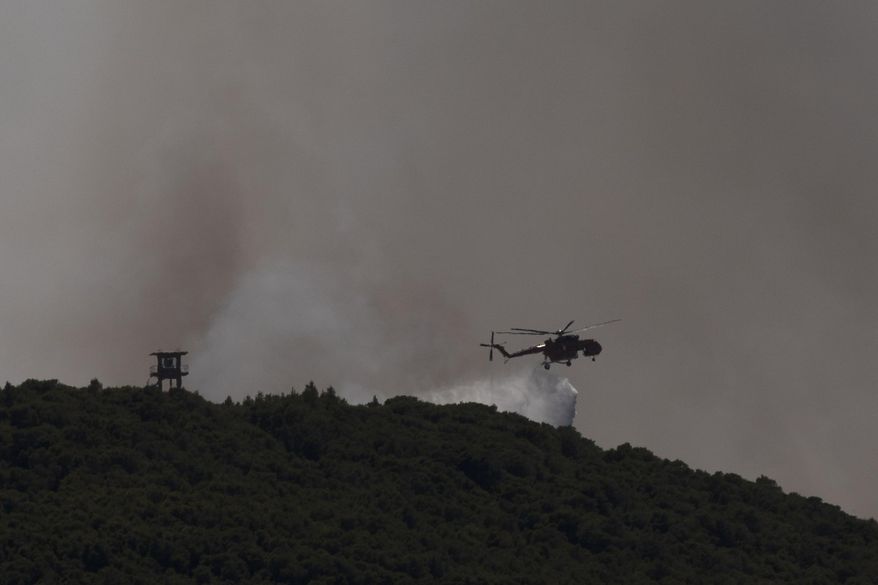 A firefighting helicopter drops water as fire burns outside the port town of Lavrio, some 60 kilometers (37 miles) south of the Athens, on Thursday, July 16, 2020. A children's summer camp and dozens of homes have been evacuated due to a wildfire south of Athens, where high winds hampered an effort to contain the blaze. (AP Photo/Petros Giannakouris)