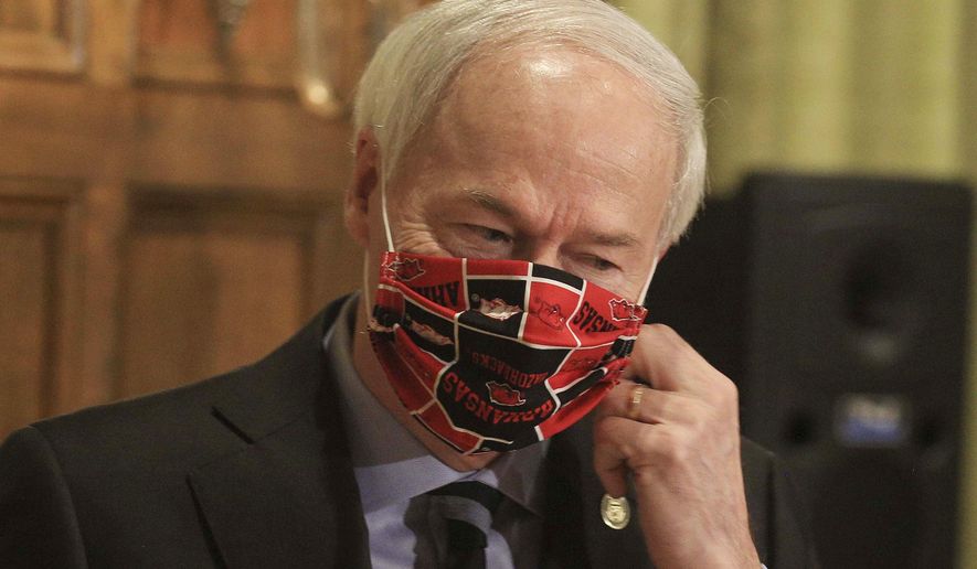 FILE - In this April 27, 2020 file photo, Gov. Asa Hutchinson takes off his Arkansas Razorbacks facemark as he arrives for the daily coronavirus briefing at the state Capitol in Little Rock. Hutchinson issued the order Thursday, July, 16, 2020, effective Monday, July 20, requiring people to wear masks in public throughout the state, which is dealing with a surge in coronavirus cases. The governor issued the order after weeks of resisting such a requirement. (Staton Breidenthal/Arkansas Democrat-Gazette via AP, File)