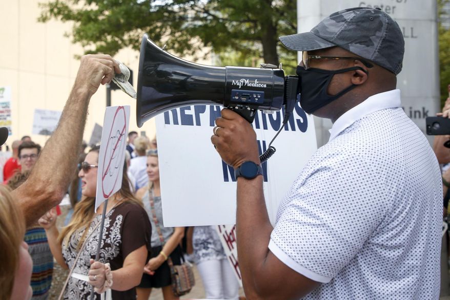 A protester puts money into a megaphone while Vernon A.M.E. Church Rev. Robert Turner speaks into the megaphone about reparations during a protest against the proposed citywide mask ordinance being voted on by the city council at Tulsa City Hall on Wednesday, July 15, 2020, in Tulsa, Okla. Turner has protested for reparations before every Tulsa City Council meeting for over a year. (Ian Maule/Tulsa World via AP)