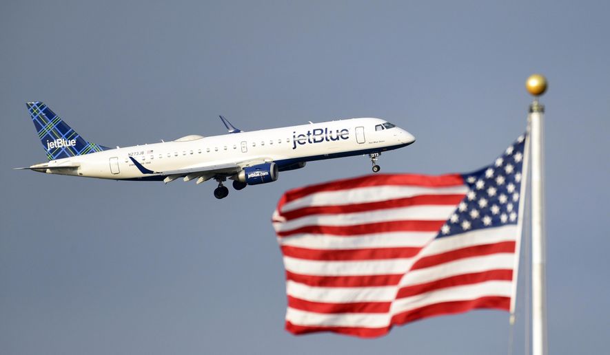 FILE - In this Sept. 21, 2018, file photo, a JetBlue plane flies past the American flag in Washington. American Airlines and JetBlue Airways said Thursday, July 16, 2020 they will sell seats on some of each other’s flights in the Northeast to strengthen both airlines in New York and Boston, where they compete against Delta and United. (AP Photo/Susan Walsh, File)