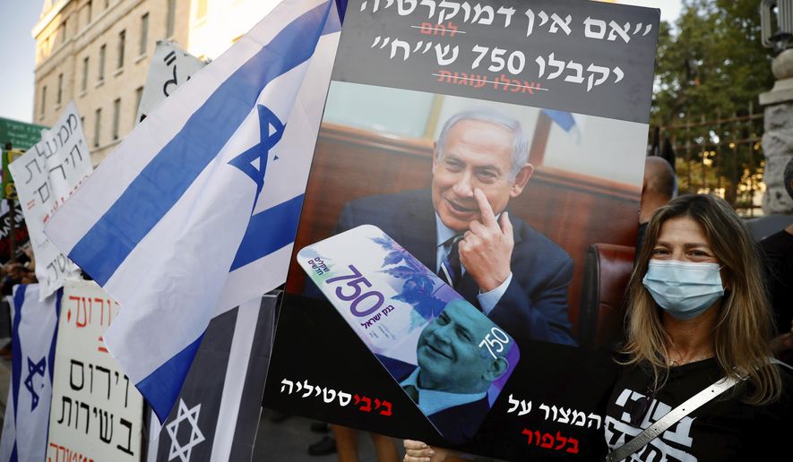 A protester holds a sign that reads "If there's no democracy, people will get 750 shekels (about $200)," in front of Prime Minister Benjamin Netanyahu's residence in Jerusalem, Thursday, July 16, 2020.Hundreds protested corruption and vented their anger at the economy. "You are out of touch, we are fed up," one poster read. (AP Photo/Ariel Schalit)