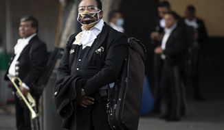 Mariachis, some wearing protective face  masks, wait for clients in Plaza Garibaldi, where residents come to hire mariachis for events and parties, in Mexico City, Friday, July 17, 2020. With large gatherings cancelled and concerns over singing inside closed spaces, work has plummeted for the hundreds of Mariachis based in Plaza Garibaldi. Those lucky enough to get occasional work say they are playing for small celebrations at home, such as birthdays or proposals, as well as at wakes for the deceased. (AP Photo/Rebecca Blackwell)