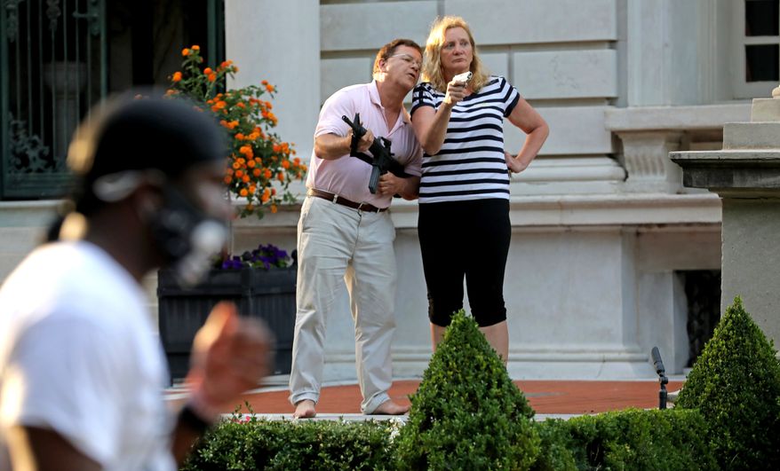 In this June 28, 2020 file photo, armed homeowners Mark and Patricia McCloskey, standing in front their house along Portland Place confront protesters marching to St. Louis Mayor Lyda Krewson's house in the Central West End of St. Louis. St. Louis’ top prosecutor told The Associated Press on Monday, July 20, 2020 that she is charging a white husband and wife with felony unlawful use of a weapon for displaying guns during a racial injustice protest outside their mansion. (Laurie Skrivan/St. Louis Post-Dispatch via AP File)