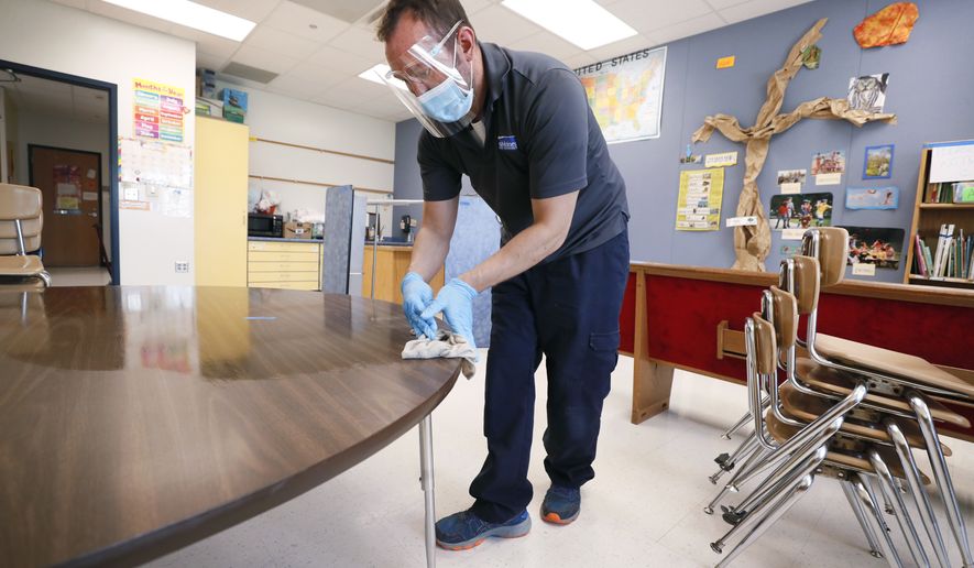 Des Moines Public Schools custodian Joel Cruz cleans a desk in a classroom at Brubaker Elementary School, Wednesday, July 8, 2020, in Des Moines, Iowa. School districts that plan to reopen classrooms in the fall are wrestling with whether to require teachers and students to wear face masks. In Iowa, among other places, where Democratic-leaning cities like Des Moines and Iowa City have required masks to curb the spread of the coronavirus, while smaller, more conservative communities have left the decision to parents. (AP Photo/Charlie Neibergall)  **FILE**