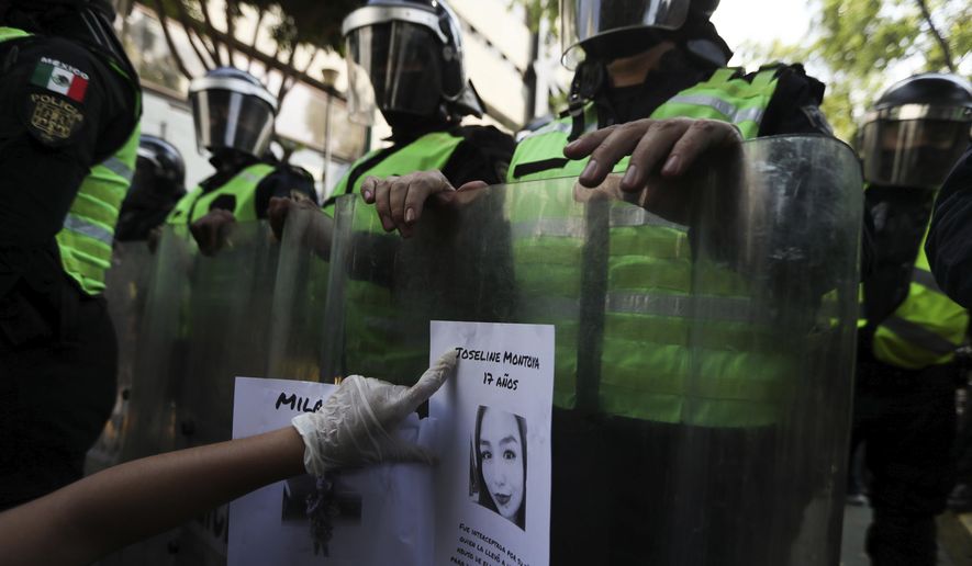 FILE - In this June 7, 2020 file photo, a demonstrator sticks a flyer of a women who was a victim of violence on the riot shield of police officer outside Mexico City's security headquarters during a protest amid the COVID-19 pandemic in Mexico City. New government figures show the number of homicides in Mexico has grown during the new coronavirus pandemic, including a 9.2% spike in killings of women, according to data released Monday, July 20. (AP Photo/Fernando Llano, File)