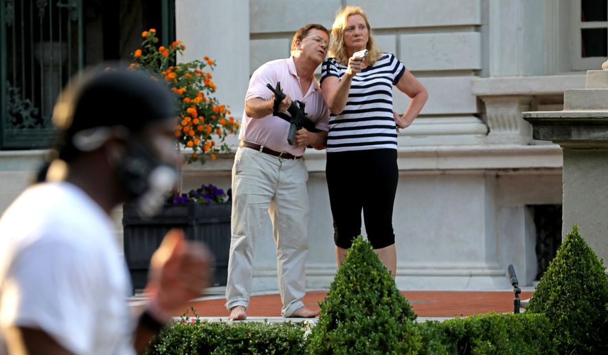 FILE - In this June 28, 2020 file photo, armed homeowners Mark and Patricia McCloskey, standing in front their house along Portland Place confront protesters marching to St. Louis Mayor Lyda Krewson's house in the Central West End of St. Louis. St. Louis’ top prosecutor told The Associated Press on Monday, July 20, 2020 that she is charging a white husband and wife with felony unlawful use of a weapon for displaying guns during a racial injustice protest outside their mansion. (Laurie Skrivan/St. Louis Post-Dispatch via AP File)