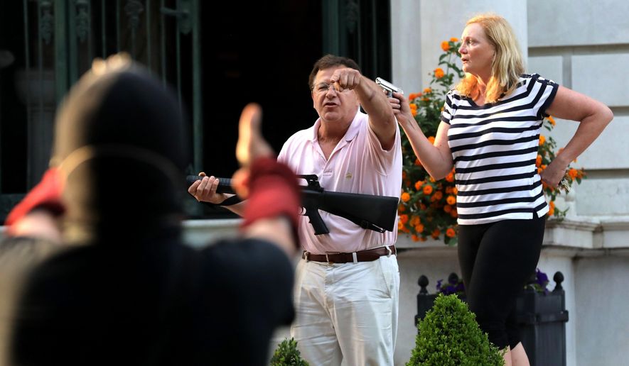 In this June 28, 2020 file photo, armed homeowners Mark and Patricia McCloskey, standing in front their house along Portland Place confront protesters marching to St. Louis Mayor Lyda Krewson&#39;s house in the Central West End of St. Louis. St. Louis’ top prosecutor told The Associated Press on Monday, July 20, 2020 that she is charging a white husband and wife with felony unlawful use of a weapon for displaying guns during a racial injustice protest outside their mansion. (Laurie Skrivan/St. Louis Post-Dispatch via AP File)