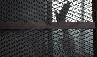 FILE - In this Aug. 22, 2015 file photo, a Muslim Brotherhood member waves his hand from a defendants cage in a courtroom in Torah prison, southern Cairo, Egypt. A leading human rights group says the coronavirus has struck several Egyptian prisons and killed several detainees, as authorities seek to stifle news of the virus’s spread behind bars. Human Rights Watch, released an extensive report Monday, July 20, 2020 documenting multiple cases of detainees who died after experiencing virus symptoms without being tested or receiving adequate medical treatment. (AP Photo/Amr Nabil, File)