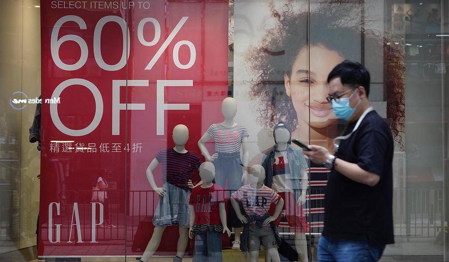 A man wearing a face mask to protect against the new coronavirus walks past a shop with sales discount sign in Hong Kong Tuesday, July 21, 2020. Hong Kong’s health officials said tighter anti-virus measures may be required if the new coronavirus infections do not come down over the next few days. (AP Photo/Vincent Yu)