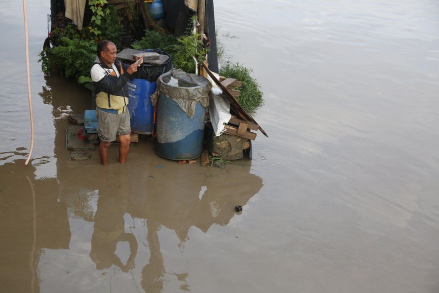 A Nepalese man takes photos of flooded Bagmati river following heavy monsoon rains in Kathmandu, Nepal, Monday, July 20, 2020. The weather department has has forecast heavy rains this week. (AP Photo/NIranjan Shrestha)