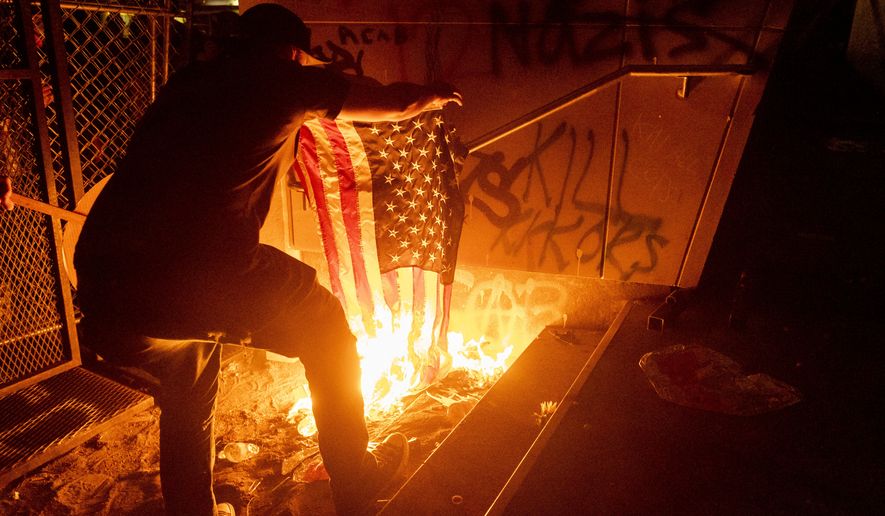 A Black Lives Matter protester burns an American flag outside the Mark O. Hatfield United States Courthouse on Monday, July 20, 2020, in Portland, Ore.  (AP Photo/Noah Berger)