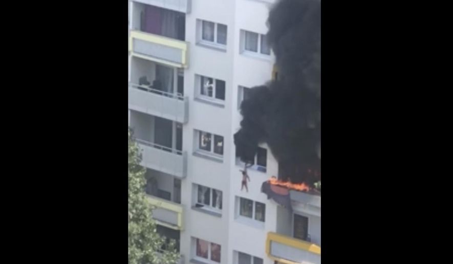 In this grab taken from video, a boy hangs from a window as flames engulfed an apartment as onlookers below prepare to catch him, in Grenoble, France, Tuesday, July 21, 2020. A boy and a toddler escaped a blaze at an apartment in the southeastern French city of Grenoble on Tuesday after they jumped into the arms of residents. The two brothers, aged three and 10 years old, were hanging from a window as flames engulfed their home and onlookers below screamed for them to jump down. (AP)