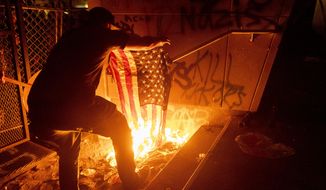 A Black Lives Matter protester burns an American flag outside the Mark O. Hatfield United States Courthouse on Monday, July 20, 2020, in Portland, Ore.  (AP Photo/Noah Berger)