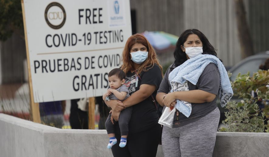 Two women and a child wait to take a Coronavirus test at a mobile testing site at the Charles Drew University of Medicine and Science Wednesday, July 22, 2020, in Los Angeles. California's confirmed coronavirus cases have topped 409,000, surpassing New York for most in the nation. (AP Photo/Marcio Jose Sanchez)