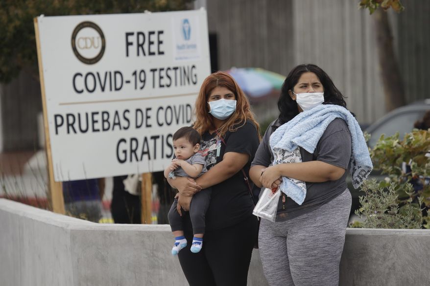 Two women and a child wait to take a Coronavirus test at a mobile testing site at the Charles Drew University of Medicine and Science Wednesday, July 22, 2020, in Los Angeles. California's confirmed coronavirus cases have topped 409,000, surpassing New York for most in the nation. (AP Photo/Marcio Jose Sanchez)