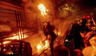 Protesters throw flaming debris over a fence at the Mark O. Hatfield United States Courthouse on Wednesday, July 22, 2020, in Portland, Ore. Following a larger Black Lives Matter Rally, several hundred demonstrators faced off against federal officers at the courthouse. (AP Photo/Noah Berger)