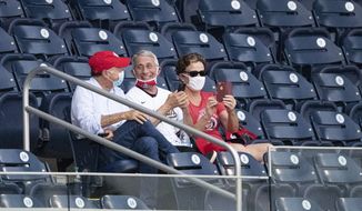 Dr. Anthony Fauci, director of the National Institute of Allergy and Infectious Diseases, center, smiles as he watches an opening day baseball game between the Washington Nationals and the New York Yankees at Nationals Park, Thursday, July 23, 2020, in Washington. (AP Photo/Alex Brandon)