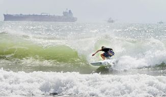 A surfer catches a barrel ride Friday, July 24, 2020, as swell waves approach the coast of South Padre Island, Texas, due to Tropical Storm Hanna approaching the Texas Gulf Coast. (Miguel Roberts/The Brownsville Herald via AP)
