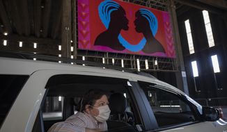 A woman takes in an art exhibit from the backseat of a car as she is driven through a warehouse displaying paintings and photos in Sao Paulo, Brazil, Friday, July 24, 2020, amid the new coronavirus pandemic. Galleries, cinemas, theaters and museums are closed due to the restrictive measures to avoid the spread of COVID-19, but a group of artists and a curator found a way to overcome the restrictions to share their art with the residents of Brazil’s largest city. (AP Photo/Andre Penner)