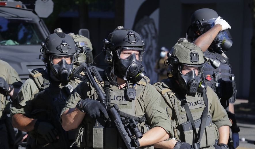 Law enforcement officers hold weapons as police clash with protesters, Saturday, July 25, 2020, during a Black Lives Matter protest near the Seattle Police East Precinct headquarters in Seattle. A large group of protesters marched Saturday in Seattle in support of Black Lives Matter and against police brutality and racial injustice. (AP Photo/Ted S. Warren)
