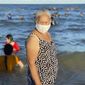 A woman wearing a face mask stands on a beach in Vung Tau city, Vietnam, Sunday, July 26, 2020. Vietnam on Sunday reimposed restrictions in one of its most popular beach destinations after a second person tested positive for the virus, the first locally transmitted cases in the country in over three months. (AP Photo/Hau Dinh)