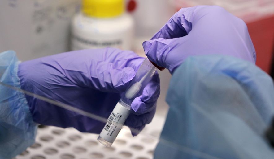 FILE - In this July 23, 2020, file photo James Robson, a biomedical engineering graduate student, holds a swab and specimen vial in the new COVID-19, on-campus testing lab at Boston University in Boston. (AP Photo/Charles Krupa, File)