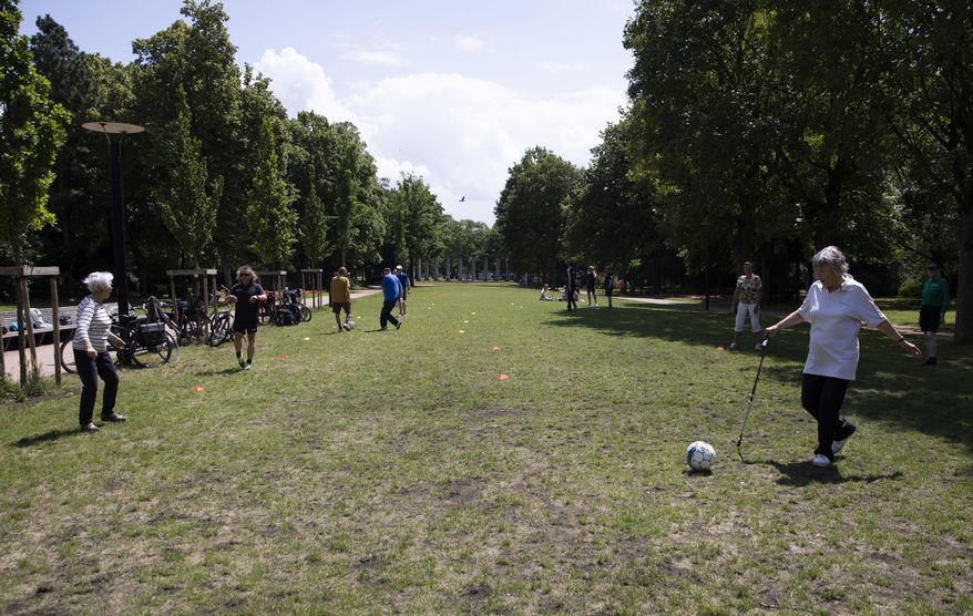 Elderly people kick a soccer ball to each other for exercise at a park in Ghent, Belgium on Friday, June 19, 2020. Belgium has lifted most of its restrictions on movement but still requires face masks on public transport and asks people to still keep a physical distance from each other, to prevent the spread of coronavirus, COVID-19. (AP Photo/Virginia Mayo)
