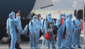 Vietnamese COVID-19 patients in protective gear, holding Vietnamese flags and carrying a portrait of the national leader Ho Chi Minh, arrive at the Noi Bai airport in Hanoi, Vietnam, on Wednesday, July 29, 2020. The 129 patients who were working in Equatorial Guinea are brought home in a repatriation flight for treatment of the coronavirus. (Tran Huy Hung/VNA via AP)