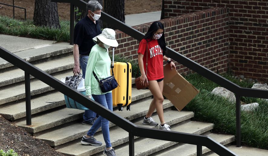 Charles Jacocks, rear, along with his wife Carrie and incoming freshman Ann Grace, right, carry their belongings as college students begin moving in for the fall semester at N.C. State University in Raleigh, N.C., Friday, July 31, 2020. The first wave of college students returning to their dorms aren’t finding the typical mobs of students and parents. At N.C. State, the return of students was staggered over 10 days and students were greeted Friday by socially distant volunteers donning masks and face shields. (AP Photo/Gerry Broome)