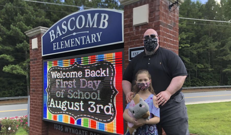 John Barrett and his daughter Autumn pose for photos outside Bascomb Elementary School in Woodstock, Ga., Thursday, July 23, 2020. Barrett says he will educate his daughter virtually and keep her out of in-person classes in Cherokee County schools, even though he's worried she will fall behind on her special education plans, because of concerns about COVID-19's spread. Cherokee County, near Atlanta, is one of many districts nationwide that gave parents a choice between in-person and all-online classes this fall. (AP Photo/Jeff Amy)