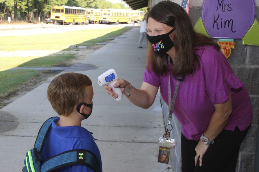 In a photo provided by Newton County Schools, teaching assistant Crystal May talks to kindergarten student Lewis Henry Thompson, 5, as she takes his temperature at Newton County Elementary School in Decatur, Miss., Monday, Aug. 3, 2020. (Janine Vincent/Newton County Schools via AP)