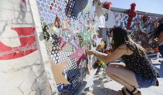 Leah Carrasco ties an orange ribbon to the Ponder Park memorial on the one year anniversary of the Walmart mass shooting Monday, Aug. 3, 2020, in El Paso. A gunman opened fire at a Walmart in El Paso killing 23 and injuring several others Aug. 3, 2019.  (Briana Sanchez/The El Paso Times via AP)