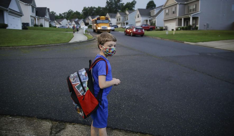 Paul Adamus, 7, waits at the bus stop for the first day of school on Monday, Aug. 3, 2020, in Dallas, Ga. Neighboring states arrived at differing conclusions on who’s in charge of the reopening of schools. The differences in philosophy underscore some of the difficulties facing states as they grapple with how to proceed amid growing coronavirus infections in numerous states. (AP Photo/Brynn Anderson)