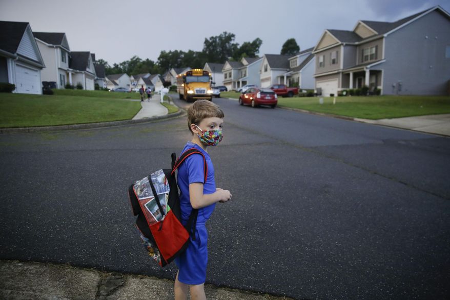 Paul Adamus, 7, waits at the bus stop for the first day of school on Monday, Aug. 3, 2020, in Dallas, Ga. Neighboring states arrived at differing conclusions on who’s in charge of the reopening of schools. The differences in philosophy underscore some of the difficulties facing states as they grapple with how to proceed amid growing coronavirus infections in numerous states. (AP Photo/Brynn Anderson)