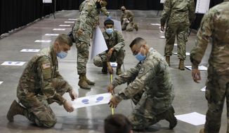 Members of the Nevada National Guard install social distancing stickers while setting up a new temporary coronavirus testing site Monday, Aug. 3, 2020, in Las Vegas. (AP Photo/John Locher)