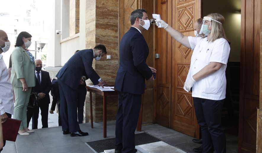 The deputy Naser Nuredini, center, of the ethnic Albanian party DUI, stands for temperature check up before entering the parliament building for the constitutive session of the Parliament, in Skopje, North Macedonia, Tuesday, Aug. 4, 2020. North Macedonia has constituted its new parliament on Tuesday with strict protocols due to COVID-19 pandemic, with parties involved in July 15 snap elections now to start a complicated power-sharing negotiations after none of the main runners have won a needed majority in a 120-member parliament. (AP Photo/Boris Grdanoski)