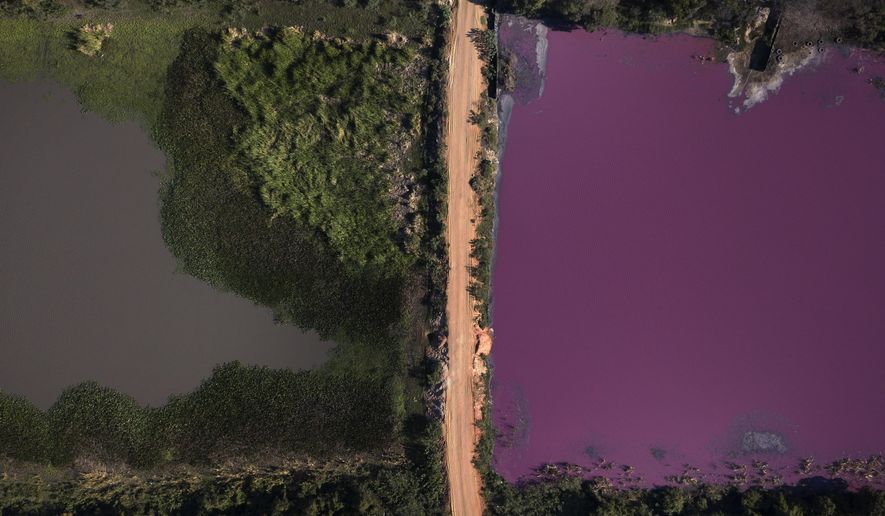 A road divides the Cerro Lagoon, where the water at right is colored and the Waltrading S.A. tannery stands on the bank, top right, in Limpio, Paraguay, Wednesday, Aug. 5, 2020. According to Francisco Ferreira, a technician at the National University Multidisciplinary Lab. who is taking water samples at the site on Wednesday, the color of the water is due to the presence of heavy metals like chromium, commonly used in the tannery process. (AP Photo/Jorge Saenz)