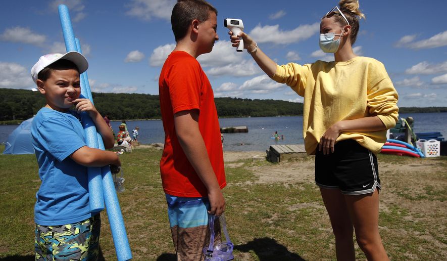 As a precaution to help prevent the spread of coronavirus, beach attendant Danielle McClure takes the temperature of Colten Ryan before allowing him and his brother, Finn, left, to enter Maranacook Beach, Wednesday, Aug. 5, 2020, in Winthrop, Maine. (AP Photo/Robert F. Bukaty)