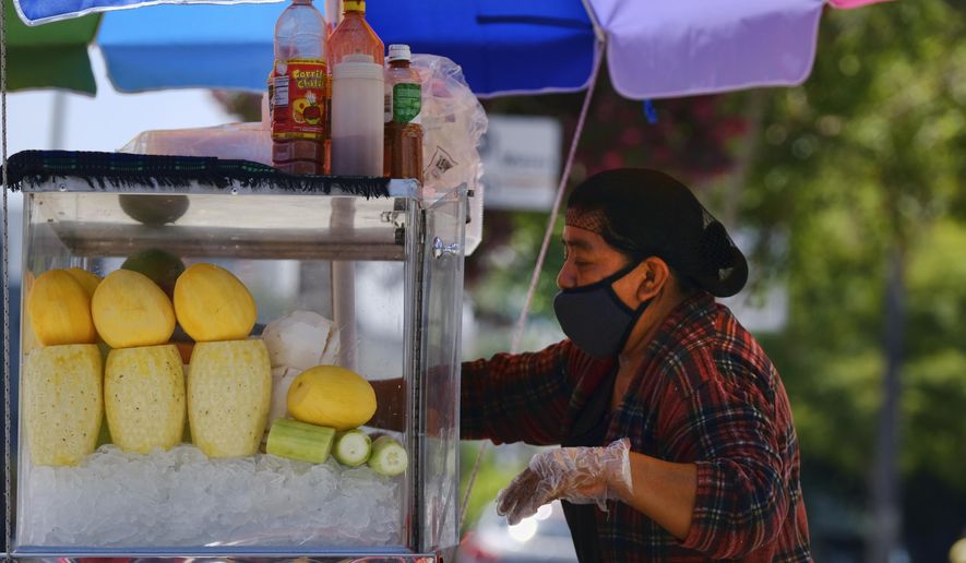 A masked fruit vendor prepares her streetside cart while waiting for customers near downtown Los Angeles on Wednesday, Aug. 5, 2020. California lawmakers are considering requiring employers to notify workers and public health officials about positive COVID-19 cases in the workplace. Violators could be charged with a misdemeanor and assessed a fine of up to $10,000. Supporters say the bill is necessary to protect workers. But business groups say the bill is so vague it will be impossible to comply with. (AP Photo/Richard Vogel)