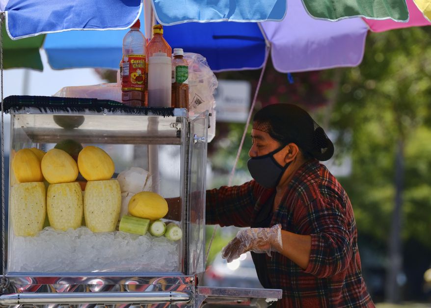 A masked fruit vendor prepares her streetside cart while waiting for customers near downtown Los Angeles on Wednesday, Aug. 5, 2020. California lawmakers are considering requiring employers to notify workers and public health officials about positive COVID-19 cases in the workplace. Violators could be charged with a misdemeanor and assessed a fine of up to $10,000. Supporters say the bill is necessary to protect workers. But business groups say the bill is so vague it will be impossible to comply with. (AP Photo/Richard Vogel)