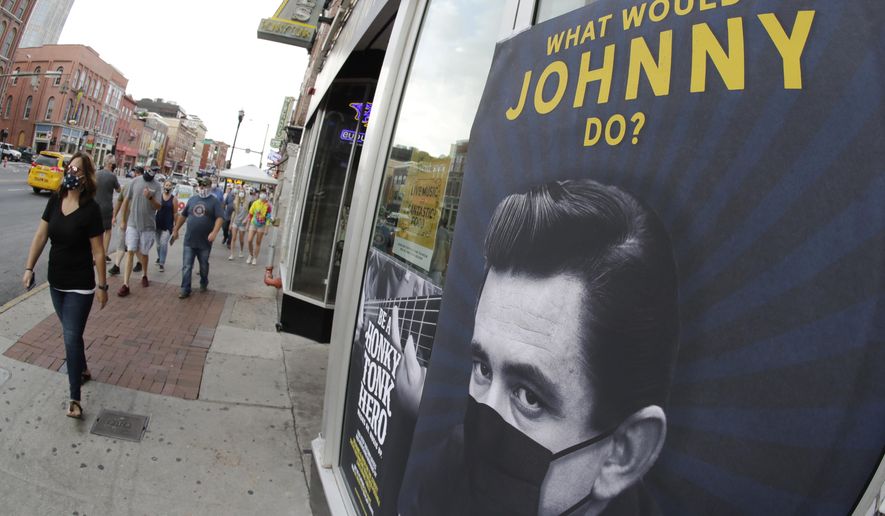 A poster showing country music legend Johnny Cash wearing a mask is attached to a storefront Wednesday, Aug. 5, 2020, in Nashville, Tenn. The wearing of face coverings is required in most public indoor and outdoor situations in Nashville due to an increase of COVID-19 cases. (AP Photo/Mark Humphrey)