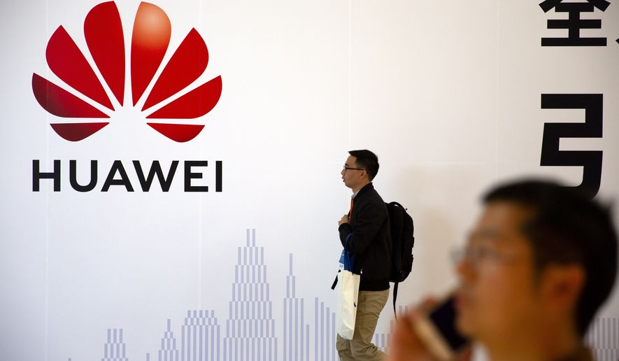 In this Oct. 31, 2019 photo, man uses his smartphone as he stands near a billboard for Chinese technology firm Huawei at the PT Expo in Beijing. Chinese tech giant Huawei kept its global business growing for almost a decade while Washington piled sanctions on the company and lobbied its allies to keep the company out of telecom networks. Now, Huawei is starting to suffer in earnest as the Trump administration steps up efforts to slam the door on access to Western components and markets in a widening feud with Beijing over technology and security. (AP Photo/Mark Schiefelbein)