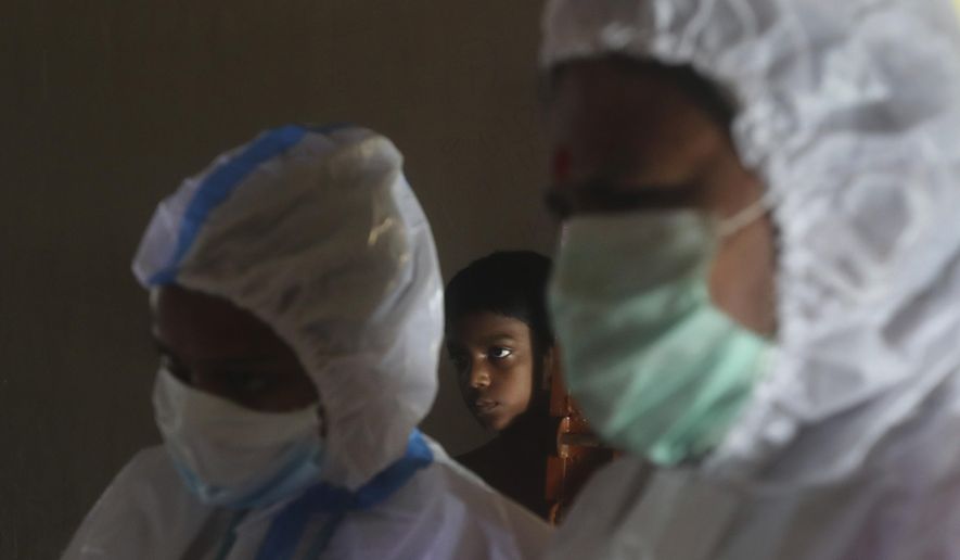A boy looks on as health workers screen people for COVID-19 symptoms at a residential building in Dharavi, one of Asia's biggest slums, in Mumbai, India, Friday, Aug. 7, 2020. As India hit another grim milestone in the coronavirus pandemic on Friday, crossing 2 million cases and more than 41,000 deaths, community health volunteers went on strike complaining they were ill-equipped to respond to the wave of infection in rural areas. (AP Photo/Rafiq Maqbool)