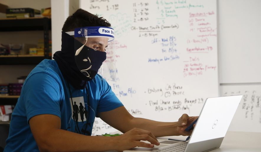 Wearing a face covering and face shield while working amid the coronavirus, Maico Olivares, lead voter registration organizer for Central Arizonans for a Sustainable Economy, works his phone and computer as he tries to reach about 25 people a day, mostly within the Latino community, to persuade them to register to vote Thursday, Aug. 6, 2020, in Phoenix. Like others who register people to vote, those efforts have become extremely difficult during the pandemic. (AP Photo/Ross D. Franklin)